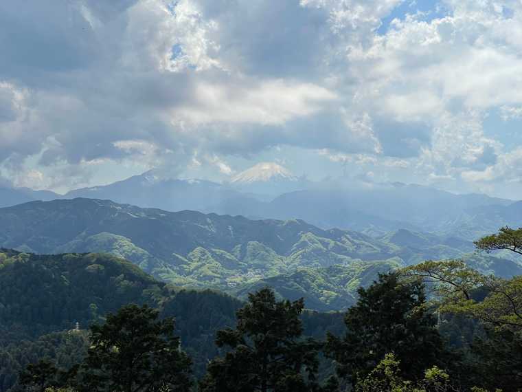"Photograph of Mt Fuji from the top of Mt Takao in Tokyo. It appears on the horizon behind another mountain range. Taken mid-April, there is still a lot of snow on Fujisan."